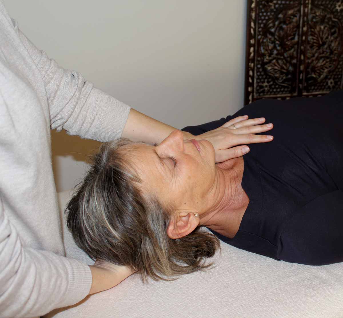 Craniosacral session taking place. Practitioner gently touches the clients head and heart area.