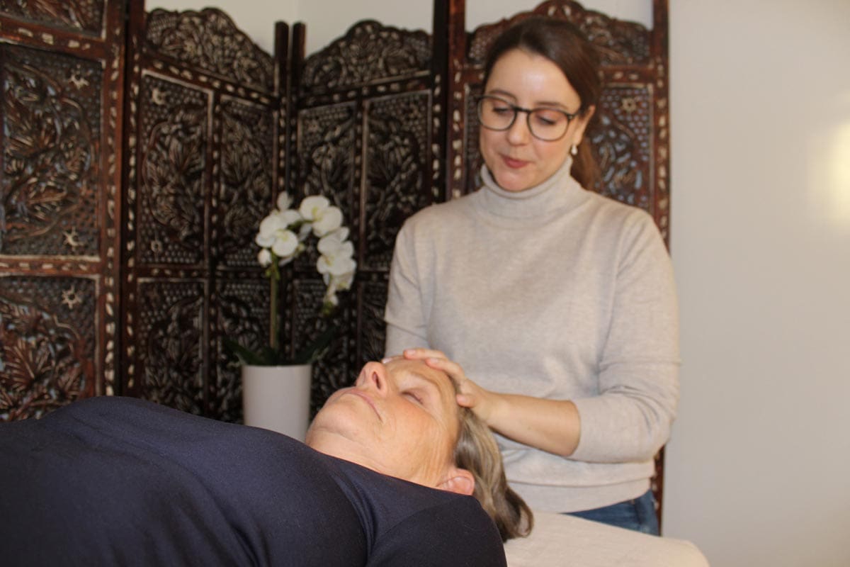 craniosacral session in action, with female therapist and client. Therapist is lightly touching clients forehead