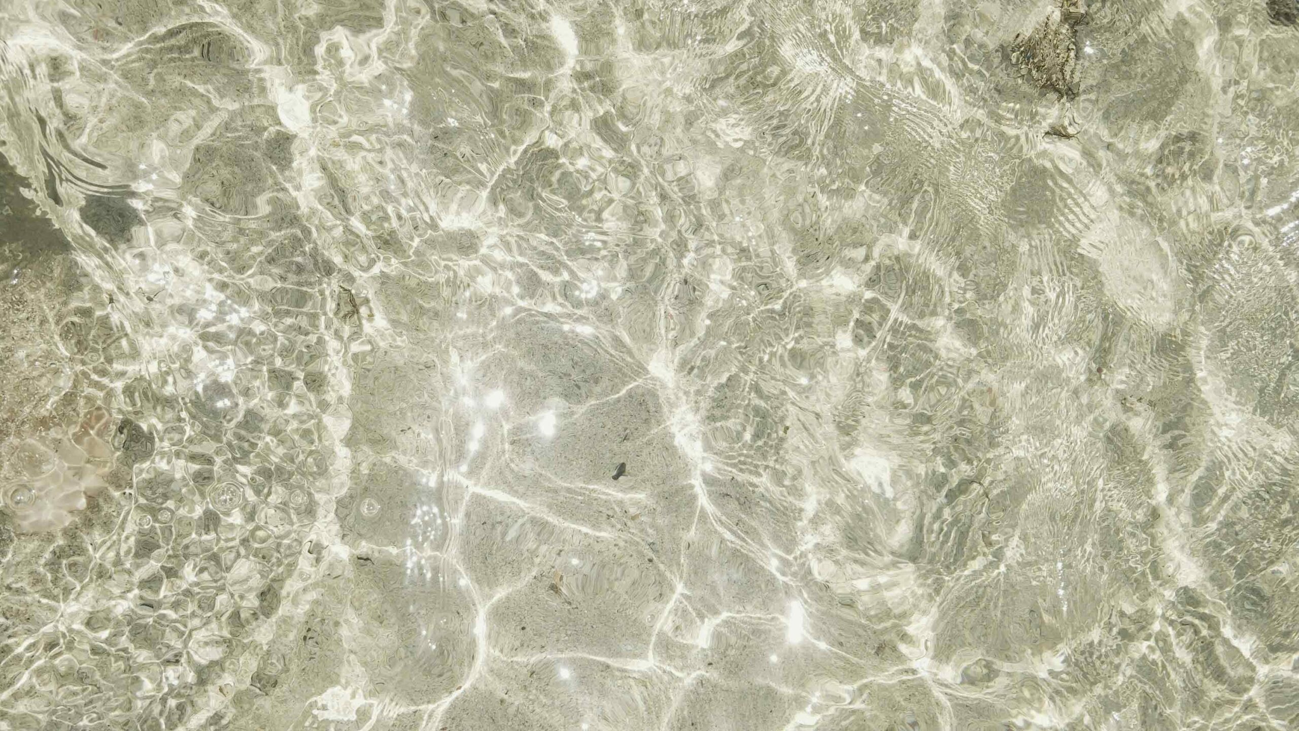 crystal clear water glittering in the sunlight, with the sandy ocean floor is seen clearly through