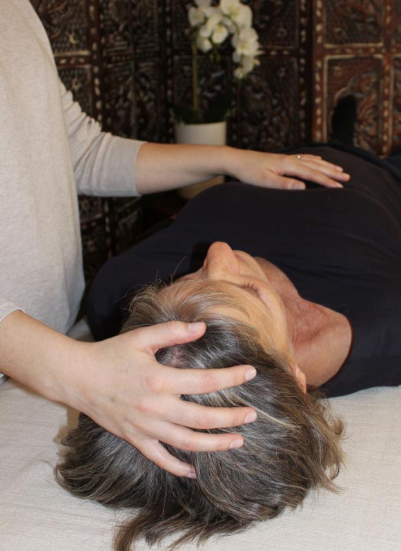 craniosacral session in action, with female therapist and client. Therapist is lightly touching clients forehead